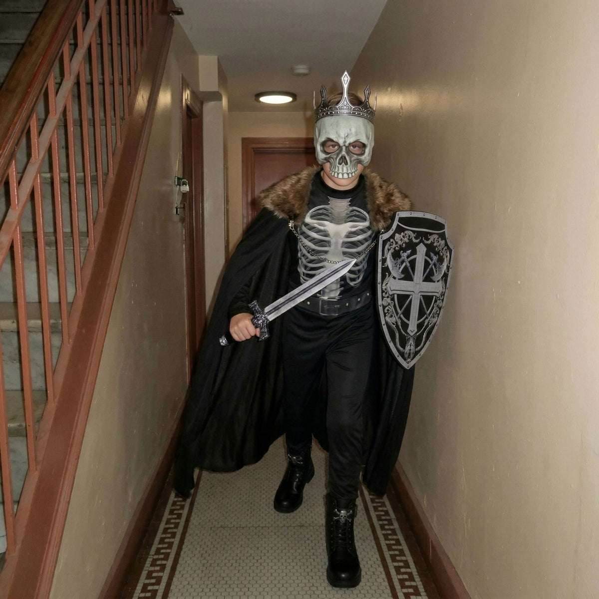 Boy wearing MCROONS Skeleton Knight Halloween costume with cloak, mask, and sword, ready for trick-or-treating.